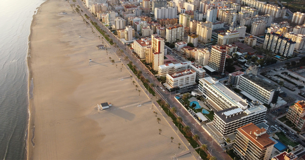 investir_gandia Plage de Gandia avec son sable doré, des palmiers en bordure, et une mer bleue calme sous un ciel dégagé, capturant l'ambiance méditerranéenne typique.