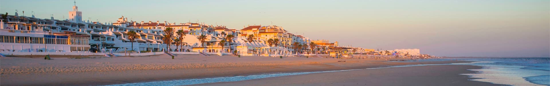 Plage de Huelva au coucher du soleil, avec des maisons blanches illuminées par une lumière dorée