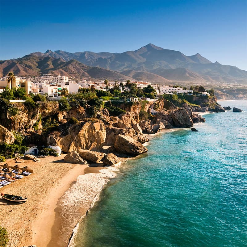 Plage de Nerja Plage pittoresque de Nerja bordée de falaises, avec des montagnes en arrière-plan et des eaux cristallines