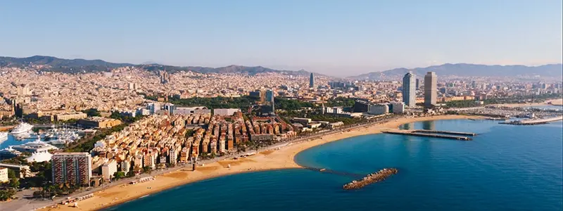 Vue de la plage de la Barceloneta à Barcelone avec son sable doré, des baigneurs et la promenade animée bordée de palmiers et restaurants.