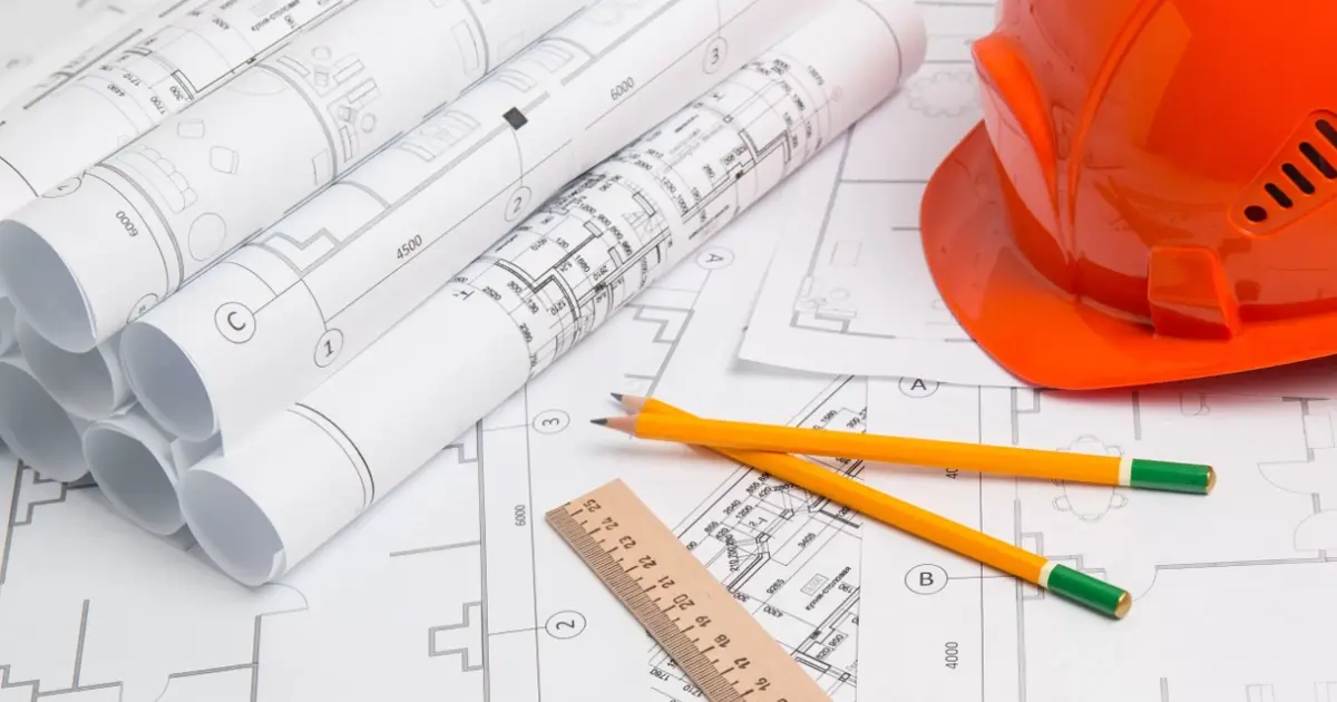 Plans d’architecte et casque de chantier posés sur des dessins techniques du cadastre, symbolisant la gestion et l’aménagement immobilier en Espagne.