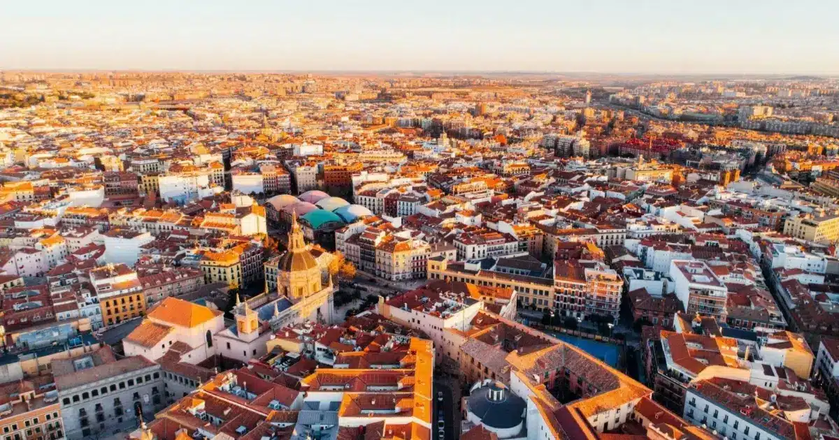 Vue panoramique aérienne de Madrid au coucher du soleil, mettant en valeur les toits rouges et l'architecture dense du centre-ville historique.