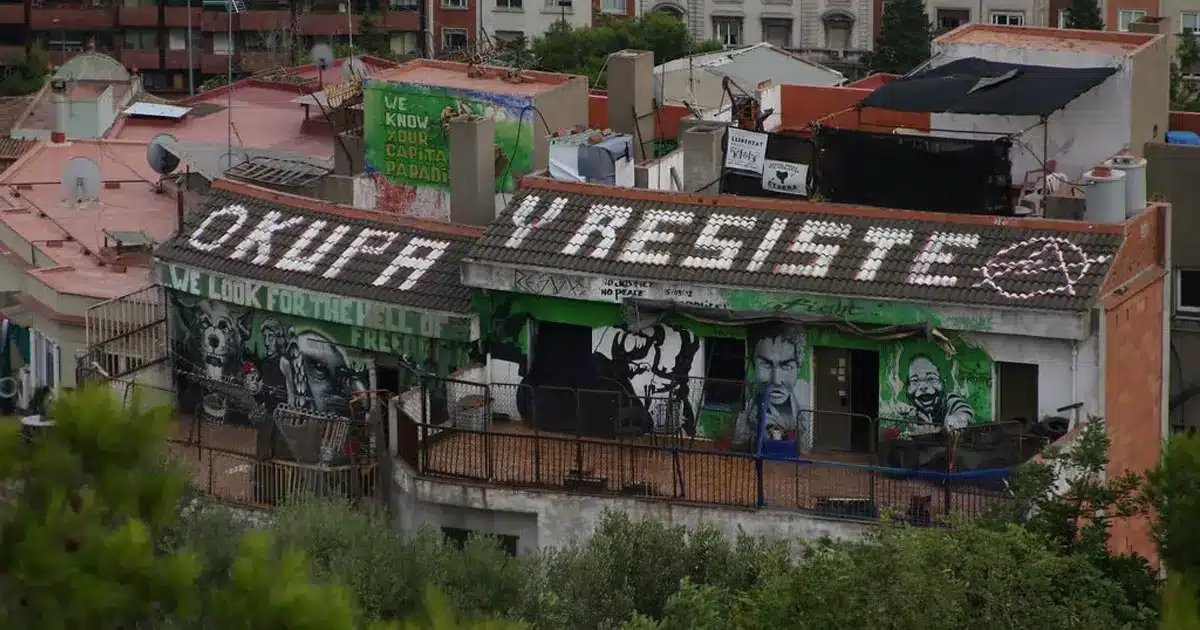 Toit d’un bâtiment occupé à Barcelone avec des graffitis militants, notamment le slogan « Okupa y resiste » (« Occupe et résiste »), illustrant le mouvement des squatters en Espagne.