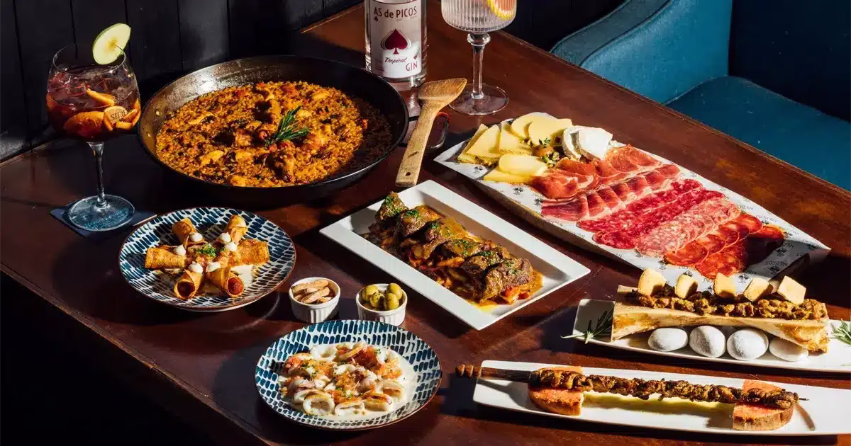 paella-tapas-charcuterie-cuisine-espagnole Table garnie de spécialités espagnoles avec paella, tapas, charcuterie et fromage, accompagnés de cocktails