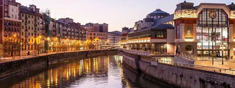 bilbao-investissement-immobilier-espagne-2026 Vue sur le centre-ville et la rivière de Bilbao au crépuscule, ville du nord d’Espagne au marché immobilier stable et attractif