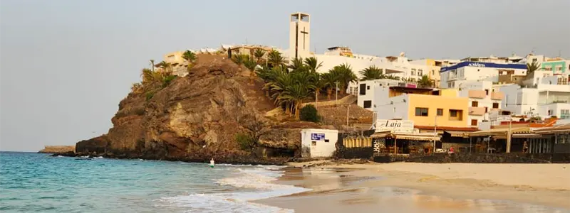 fuerteventura-investissement-immobilier-iles-canaries-2026 Plage dorée et village côtier à Fuerteventura, îles Canaries — un lieu privilégié pour investir dans l’immobilier locatif en 2026