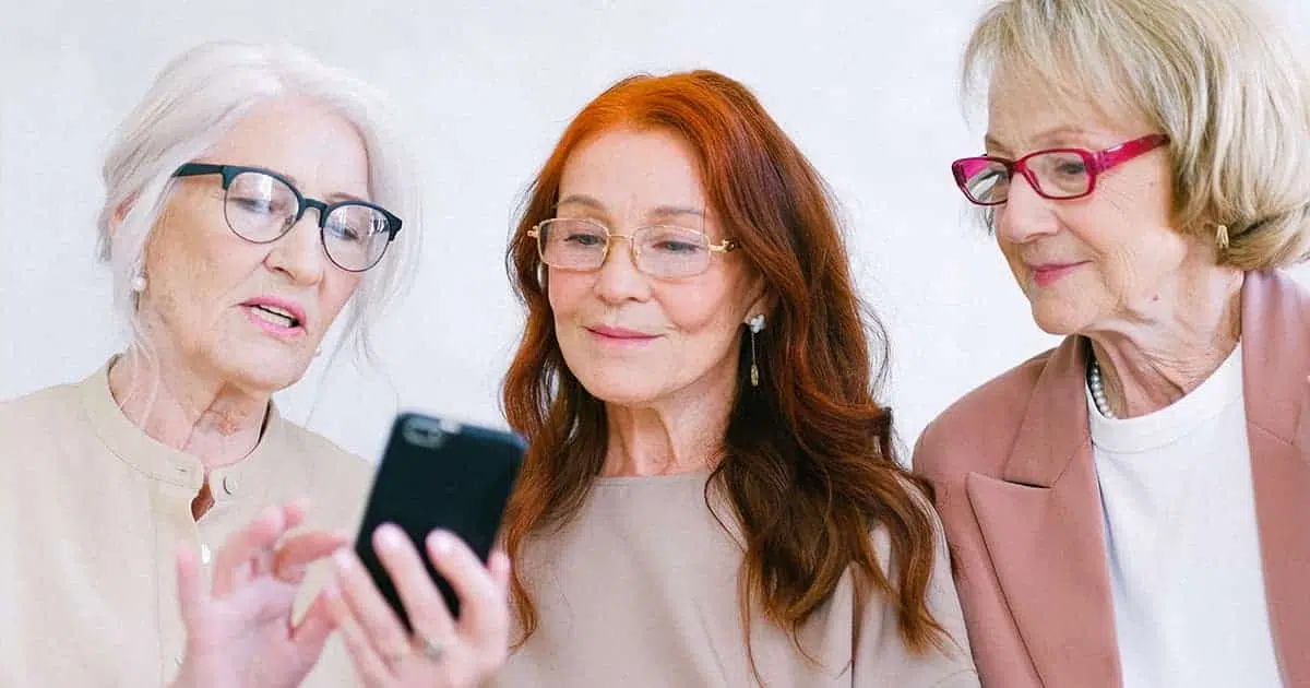 Trois femmes seniors consultant un smartphone ensemble, illustrant des repères économiques plus accessibles et un coût de la vie maîtrisé par rapport aux grandes villes françaises.